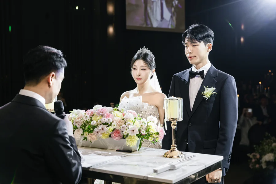 주례 앞에 나란히 선 신랑신부, 뒤편 스크린에 실시간 화면이 비친 모습