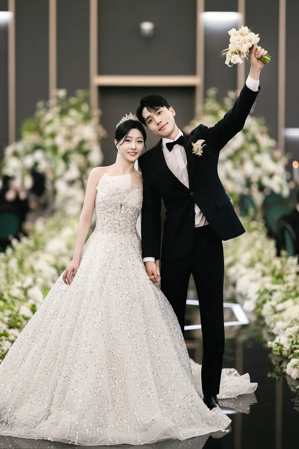 부케를 치켜든 신랑 옆에서 미소 짓는 신부, 플라워로드 배경 전신컷